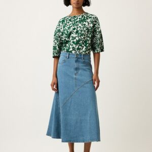 Model wearing Nancybird Aurora Skirt in denim—A‑line midi skirt with waist tie, front slant patch pockets, contrast stitching and slit back