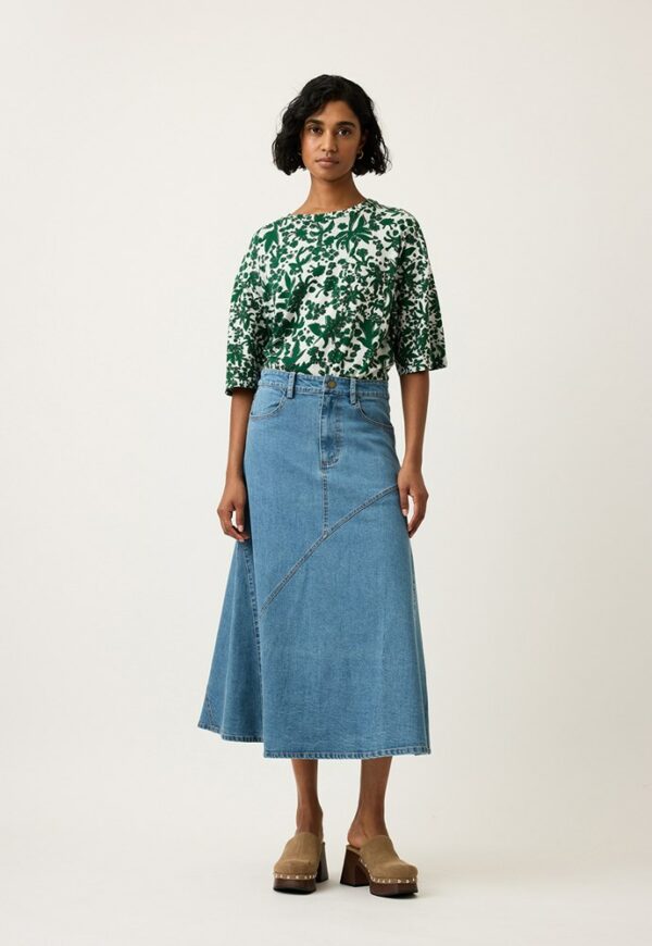 Model wearing Nancybird Aurora Skirt in denim—A‑line midi skirt with waist tie, front slant patch pockets, contrast stitching and slit back