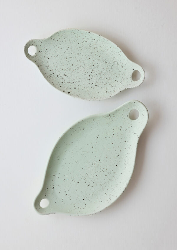 Two pistachio -colored porcelain grazing plates with sculptural curves and speckled glaze.