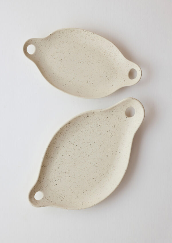 Two oatmeal -colored porcelain grazing plates with sculptural curves and speckled glaze.
