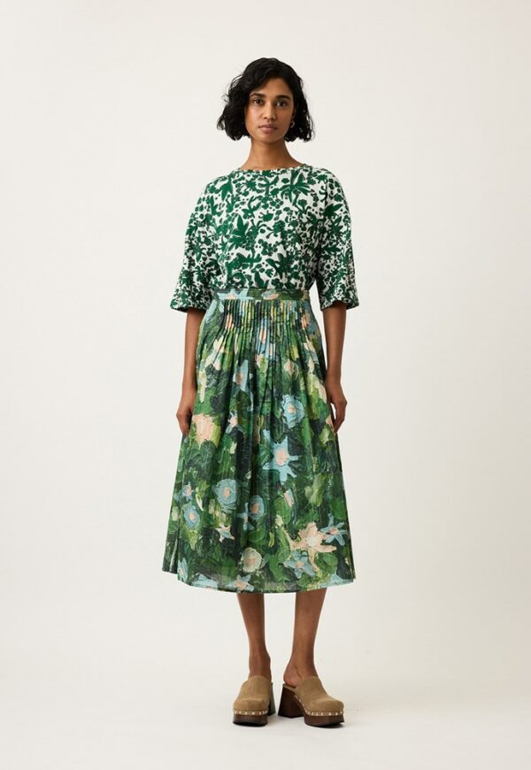 Nancybird Alma Yoke Skirt in Garden print displayed on model among flowers—lightweight cotton voile fabric, green and gold botanical pattern, midi silhouette modeled.