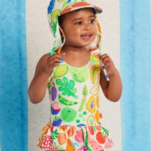 Model wears Halcyon Nights Baby Frill Bather in Eat The Rainbow print—frill-trimmed swimsuit with vibrant rainbow artwork and built-in nappy liner for babies