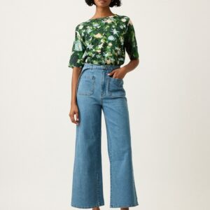 Model wearing Nancybird Briar Pants in denim—high‑waist straight‑leg jeans with self‑fabric tie belt, front and back patch pockets, and contrast top stitch detailing in mid wash denim