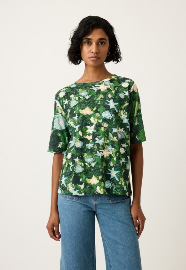 Model wearing Nancybird Grace Tee in Garden print—relaxed organic cotton crew‑neck tee featuring Emily Wright botanical artwork on light blue background