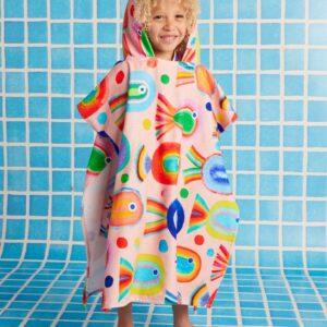 Model wears Halcyon Nights Kids Hooded Towel in Fancy Fins print—poncho-style cotton towel with hood, white underside, and colourful undersea design by Min Pin