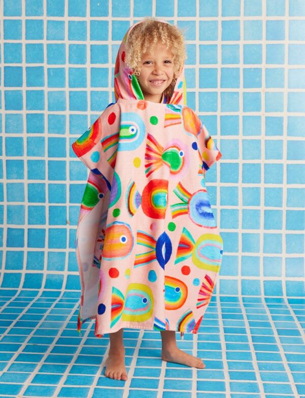 Model wears Halcyon Nights Kids Hooded Towel in Fancy Fins print—poncho-style cotton towel with hood, white underside, and colourful undersea design by Min Pin