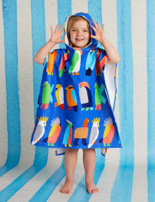 Model wears Halcyon Nights Kids Hooded Towel in Flamin' Galahs print—poncho-style cotton towel with hood, white underside, and colourful pink galahs by Min Pin