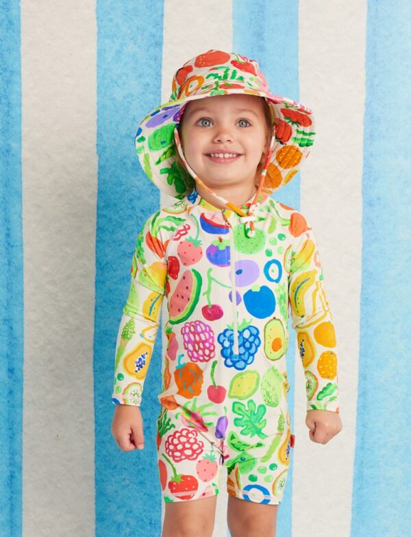 model wears Halcyon Nights Swim Bucket Hat in Eat The Rainbow print—baby swim hat with wide brim, chin ties, adjustable fit and UPF 50+ protection
