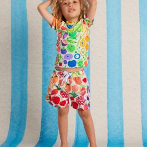 Model wears Halcyon Nights Kids Boardshorts in Eat The Rainbow print—colourful quick-dry shorts with elastic waist, drawcord, and Seeun Park’s vibrant artwork