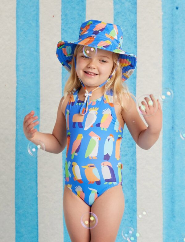 Model wears Halcyon Nights Elastic Strap Bather in Flamin’ Galahs print—one-piece swimsuit with playful pink galahs and colourful elastic straps for kids