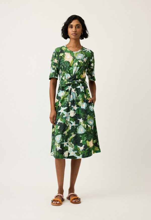 Model wears Nancybird Terra Short Sleeve Wrap Dress in Garden print—organic cotton jersey midi dress with short sleeves, crew neck, wrap tie waist and botanical green‑leaf artwork
