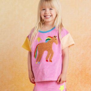 model wears Halcyon Nights Giddy Up Terry T Shirt—short sleeve kids cotton tee in soft terry fabric with cheerful horse-themed print and shoulder snap buttons