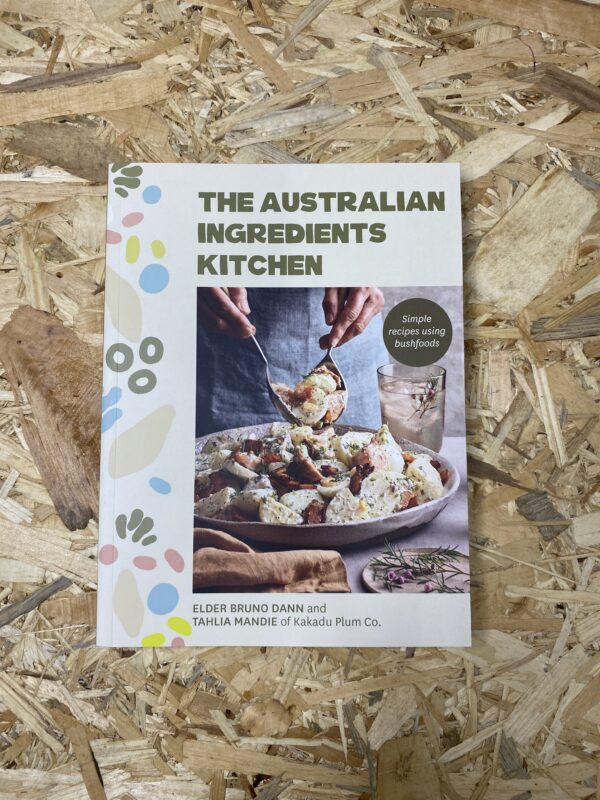Cover of The Australian Ingredients Kitchen by Elder Bruno Dann and Tahlia Mandie, featuring a vibrant array of native Australian ingredients and dishes, reflecting the book's focus on bush foods and cultural