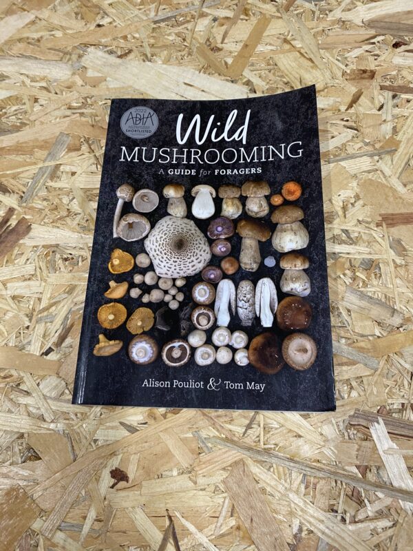 Cover of Wild Mushrooming: A Guide for Foragers by Alison Pouliot and Tom May, featuring a vibrant collage of various mushroom species set against a natural forest backdrop, reflecting the book's focus on safe and sustainable foraging practices.
