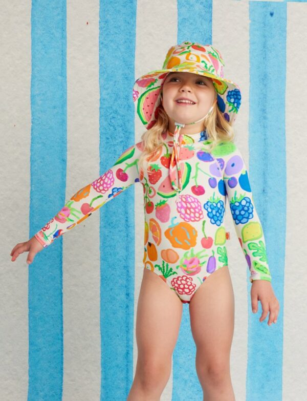 model wears Halcyon Nights Long Sleeve Zip Bather in Eat The Rainbow print—kids swimsuit with front zip, full sleeves, bright rainbow design, and UPF 50+ protection