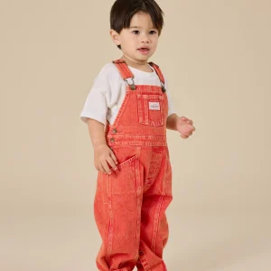 Toddler wearing Goldie & Ace Blake Vintage Washed Denim Overalls in apple red, featuring adjustable straps and leg snaps.
